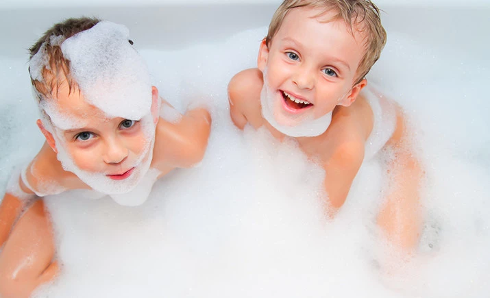 Two children are joyfully bathing, covered in bubbles.